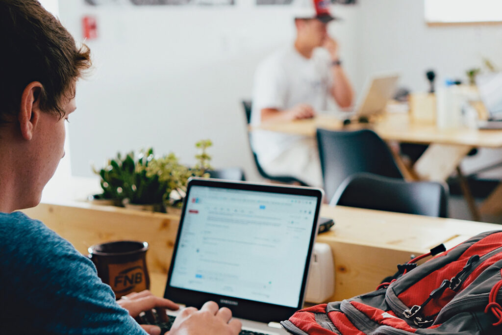alt=’A male is seated at a table in a coffee shop, working on a laptop’, aria-hidden=’true’